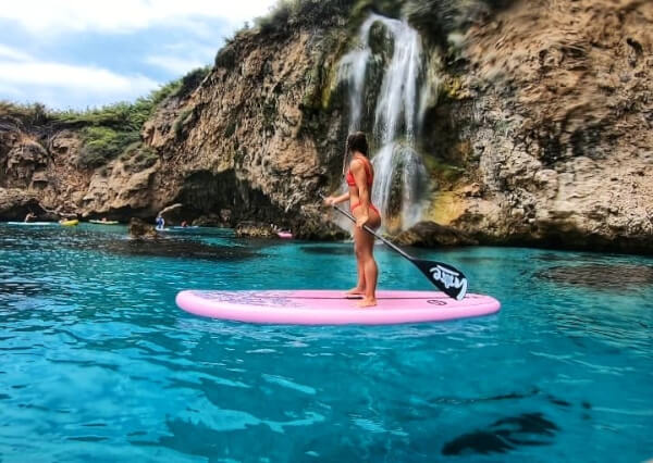 Mujer sobre tabla de paddle surf delante de la cascada de Maro Cerro Gordo en Nerja Malaga